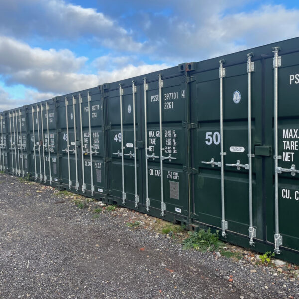 A row of green container storage units, securely locked with various load capacity information displayed